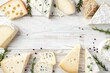 Variety of cheeses including Suluguni camembert blue cheese parmesan maasdam and brie with herbs and pepper Top view on white wooden background with empty spac