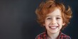 Delightful young red-haired boy with a bright toothy smile and freckles on a dark background