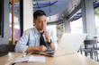 © Aria Armoko - Asian man think and look for ideas with blue shirt using laptop and mobile phone in coffee shop, online business