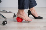 Fototapeta Zwierzęta - Business woman massages her feet on a massage ball with spikes.