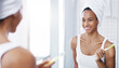 © peopleimages.com - Woman, mirror and brushing teeth in bathroom with smile or towel after shower for hygiene, cleaning or oral care. Female person, reflection and home for healthy mouth or tooth dental, gums or routine