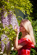 A beautiful blonde woman near a blooming wisteria on a sunny day.