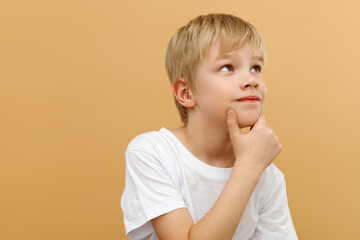 Blonde boy . Let me think . Thoughtful clever schooler in white shirt with puzzled serious expression , child thinking doubting , making choice. indoor studio shot isolated on beige background