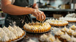 A baker is carefully spreading meringue on top of a lemon tart. The tart is sitting on a metal baking sheet.