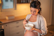 A high angle shot of a beautiful pregnant lady eating a bowl of oatmeal in a kitchen