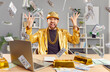 Successful excited young funny man in golden suit sitting at desk with gold bar, building online business using laptop, throwing dollar bills making money rain celebrating success or win a lottery.
