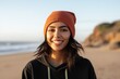 Portrait of a content indian woman in her 20s sporting a trendy beanie in front of sandy beach background
