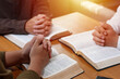 Power of hope or love, christian devotion background, bible study group concept. A group of people are gathered around a table with their hands outstretched in prayer over a Holy Bible.