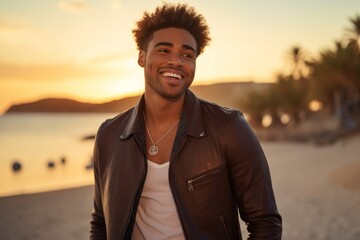 Wall Mural - Portrait of a smiling afro-american man in his 20s sporting a stylish leather blazer in front of vibrant beach sunset background