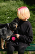 A young attractive woman with pink hair is sitting on wooden bench in spring park with her Blue Heeler. Australian cattle dog on a walk with female owner. Family dog outdoor lifestyle concept.