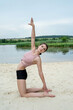 Beautiful young slim woman in sportwear practicing yoga pose by the lake