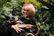 A young attractive woman with pink hair and glasses hugs with her Blue Heeler in spring park. Australian cattle dog on a walk with female owner. Family dog outdoor lifestyle concept.