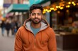 Portrait of a satisfied indian man in his 20s sporting a comfortable hoodie on vibrant market street background