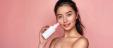 Fototapeta  - young beautiful girl with black hair and perfect smooth skin posing in front of the camera and holding a white cosmetic bottle mockup in pastel colored studio created with Generative AI Technology