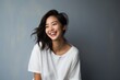Portrait of a joyful asian woman in her 20s wearing a simple cotton shirt over minimalist or empty room background