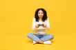 Full body little kid teen girl of African American ethnicity wears white casual clothes sits hold play pc game with joystick console isolated on plain yellow background. Childhood lifestyle concept.