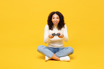 Wall Mural - Full body little kid teen girl of African American ethnicity wears white casual clothes sits hold play pc game with joystick console isolated on plain yellow background. Childhood lifestyle concept.