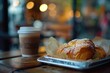 A close-up of a croissant and coffee cup on a wooden table.