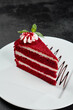 Red velvet cake on white plate on dark stone background. Popular red cake with layer biscuit and cream. Red velvet dessert in minimal style on black backdrop. Piece of cake with mint.