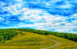 Hilly landscape with fields and blue sky. Upland view of sunny landscape with green field, winding road and blue sky with white summer clouds.
