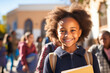 Smiling African American schoolgirl with textbooks, embracing the excitement of a new school year against the backdrop of classmates and the school building.