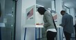 © Framestock - Muslim woman in hijab comes to vote in booth in polling station office. National Election Day in the United States. Political races of US presidential candidates. Concept of civic duty. Dolly shot.