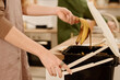 Side view of hands of young housewife opening lid of plastic bucket with compost and throwing banana peel after eating fruit
