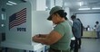 © Framestock - Female American army soldier votes in booth in polling station office. National Elections Day in the United States. Political races of US presidential candidates. Concept of civic duty. Dolly shot.