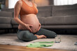 An unrecognizable pregnant woman holding her belly while working out in the living room