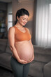 A beautiful pregnant woman holding her stomach and practicing yoga in the living room