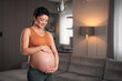 A smiling pregnant woman caressing her belly and practicing yoga in the living room