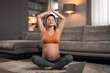 A focused adult pregnant woman meditating at home with clasped hands above her head