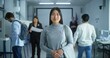 © Framestock - Portrait of Asian woman, United States of America elections voter. Woman with badge stands in modern polling station, poses, smiles, looks at camera. Background with voting booths. Civic duty concept.