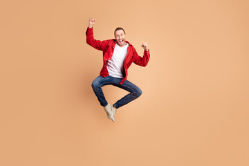 Poster - Full length portrait of nice young man raise fists jump wear red shirt isolated on beige color background