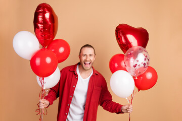 Sticker - Portrait of nice young man hold balloons wear red shirt isolated on beige color background