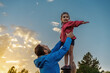 Under cloud-streaked sky, a father steadies his daughter atop a wooden stump - she points forward with determination, signaling the adventure and discovery that lies ahead.