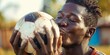 © JW Studio - Happy teenage African American football soccer boy player holding and kiss ball in the meadow with sunset background, copy space.