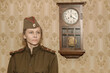 A woman in a military uniform against the background of old paper wallpaper and a clock with a pendulum.