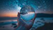 Hand holding a crystal ball with a starry night sky and a reflection of a beach inside it.