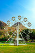 Beautiful scenic with white ferris wheel decorated with lights and small flags for fun and enjoyment of festival or carnival stand on green lawn. Outdoor theme park with beautiful nature as background