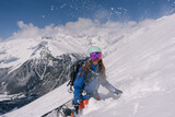 Fototapeta  - Woman snowboarder riding on slope of powdery snow in high mountains avalanche-prone area. Freeride at ski resort, Snow splashes trail,  mountain peaks view
