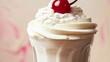 Vanilla milkshake with whipped cream topped with red cherry and shaved chocolate on pink background