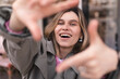 Attractive woman with a lovely smile making a frame gesture with her fingers framing her face. Woman posing on selfie photo looking at camera walking outdoors in urban cafe.