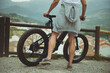 © Taras Grebinets - Cropped portrait of a young male cyclist, standing near his electric bike, having a break after biking in mountains. People. Active healthy lifestyle. E-bike as sustainable, eco friendly transport