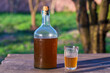 Big bottle with a drink made from fermented birch sap on the wooden table on a warm spring day, closeup. Traditional Ukrainian cold barley drink kvass in a glass jar and glass in yard