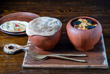Fototapeta Pomosty - Two clay pots with stewed vegetables on a wooden table, closeup. Stewing food in earthenware is considered healthy