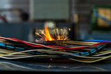 Fototapeta Pomosty - Flames, sparks, smoke between electrical cables, closeup. Short circuit in the twisted wires from the electrical devices, fire hazard concept