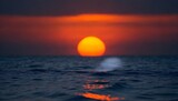 Fototapeta  - Out of focus sun setting over the ocean glowing orange with dark blue background