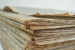 candid close-up showcasing the worn edges and faded print of old newspapers stacked together, against a white background, inviting viewers to explore the stories and headlines of t