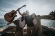 © qunica.com - Joyful friends playing guitar and having fun on a boat, embodying a relaxing weekend getaway on the lake
